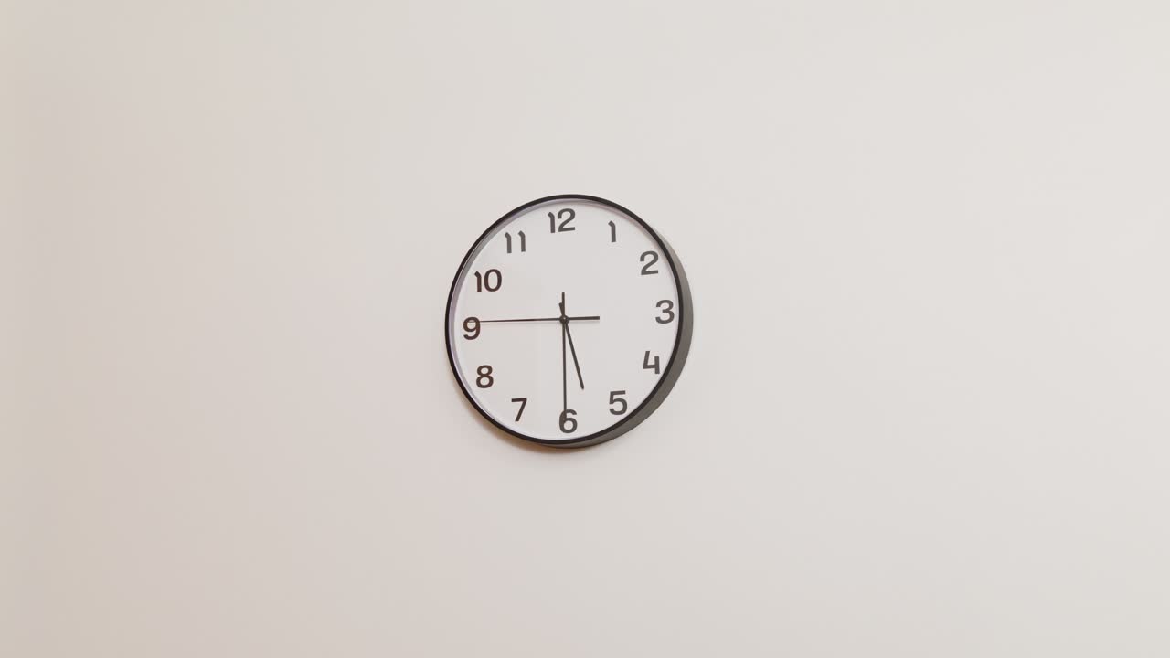 A wide 4K shot of a standard office wall clock with a black frame and white face, displaying 5:30, mounted on a plain white wall.