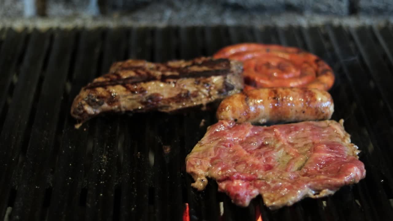 Cuts of meat and chistorra sausage roasting over charcoal