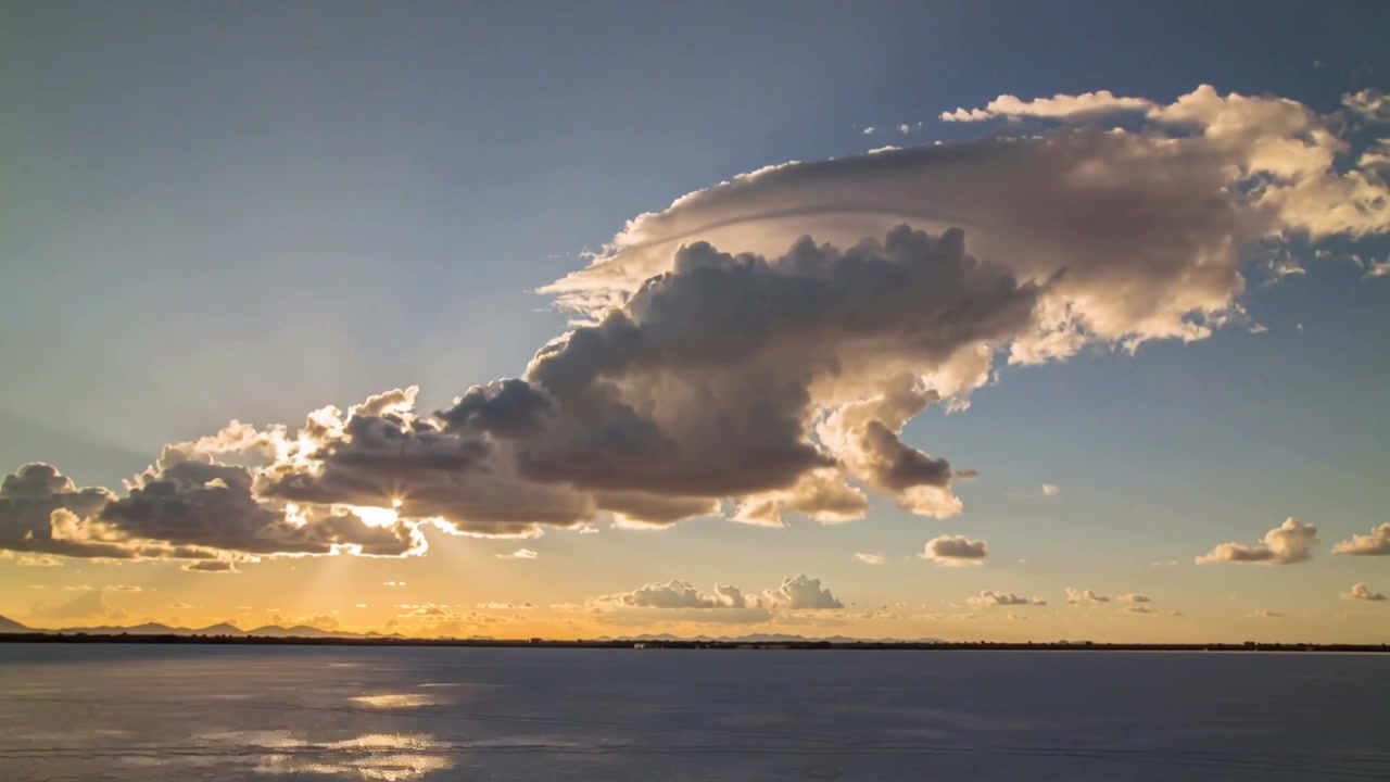 Drifting cumulus cloud moving right over salt flat, wind aloft pushing while low sun making beams
