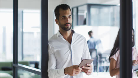 Mixed-race-businessman-standing-in-office-doorway,-using-tablet,-smiling-to-camera