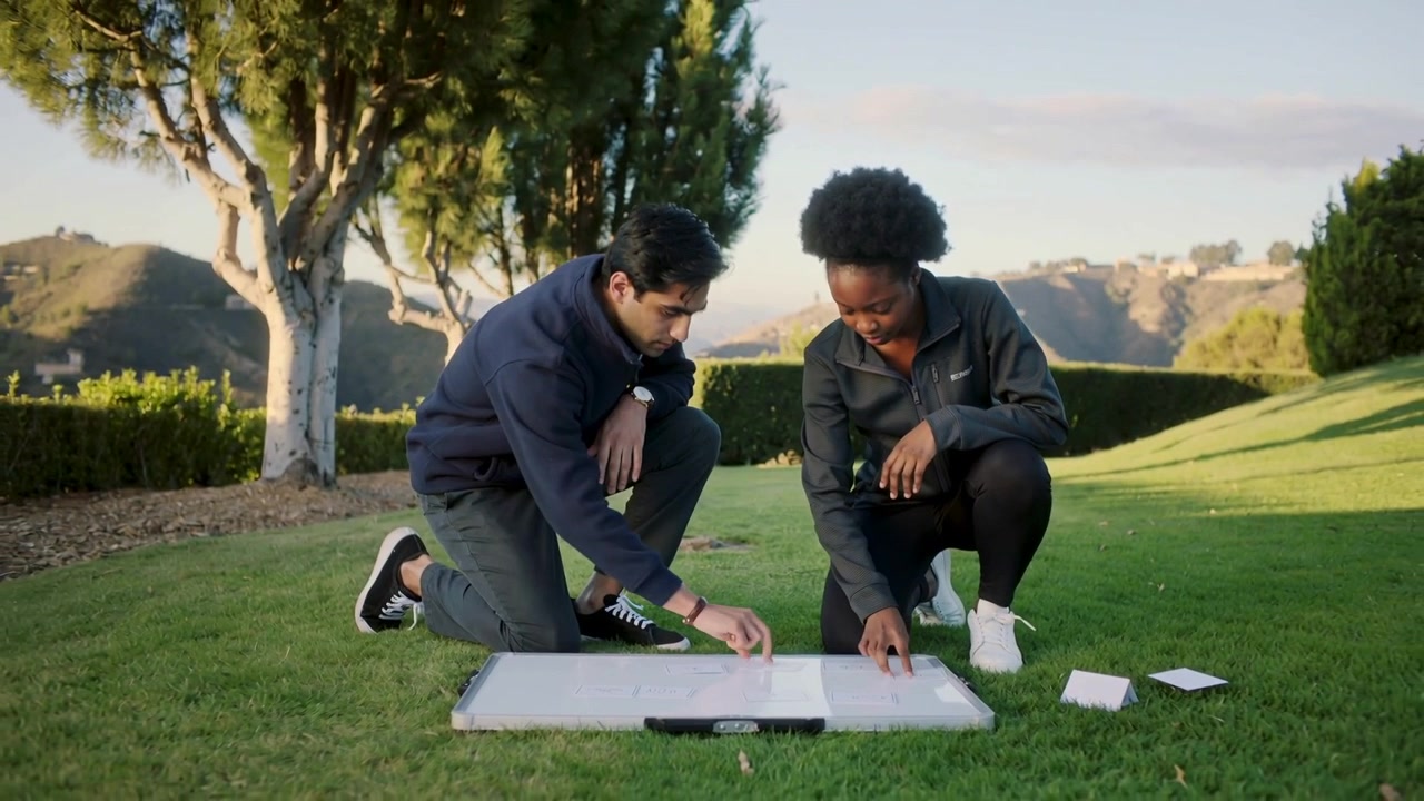 Arranging pair kneeling on park, in dark jackets, picking cards and planning layout on board handle