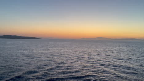 calm twilight water with gentle waves reflecting golden hour light off the coast of greece.