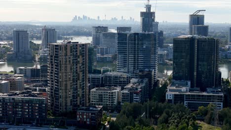 Stadterweiterung:-Glitzernde-Wolkenkratzer-Ragen-über-Dem-Fluss-Auf,-Mit-Entfernter-Stadtkulisse-Im-Morgenlicht