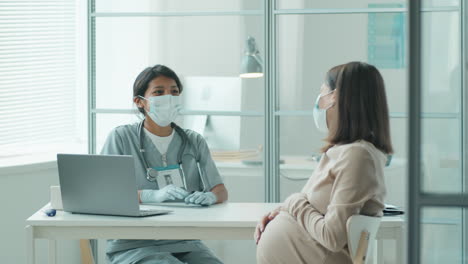 hispanic midwife in mask talking with pregnant woman