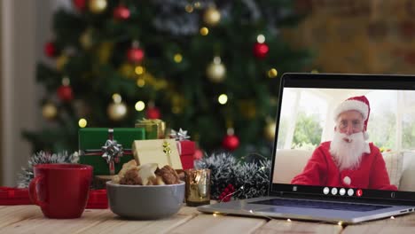 Älterer-Kaukasischer-Mann-Im-Weihnachtsmannkostüm-Bei-Videoanruf-Auf-Laptop,-Mit-Weihnachtsdekorationen-Und-Baum