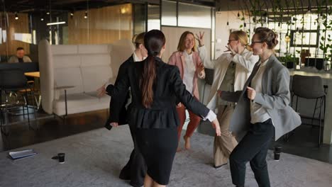 A-group-of-confident-businesswomen-in-business-suits-dance-on-a-gray-carpet-in-a-modern-office-after-success-in-business