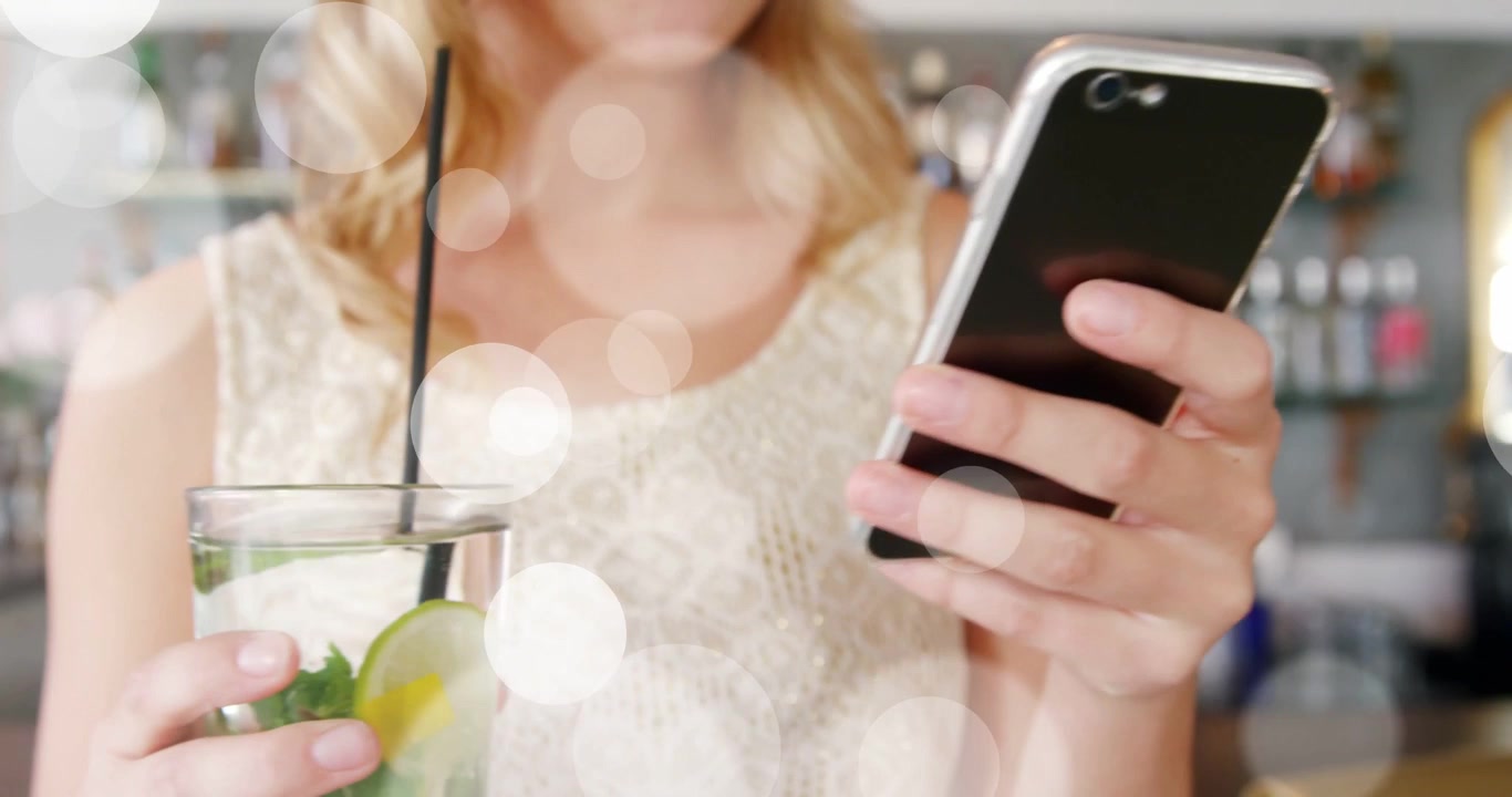 Woman tapping phone, showing lime mint glass and placing drink at bar, bokeh guiding focus