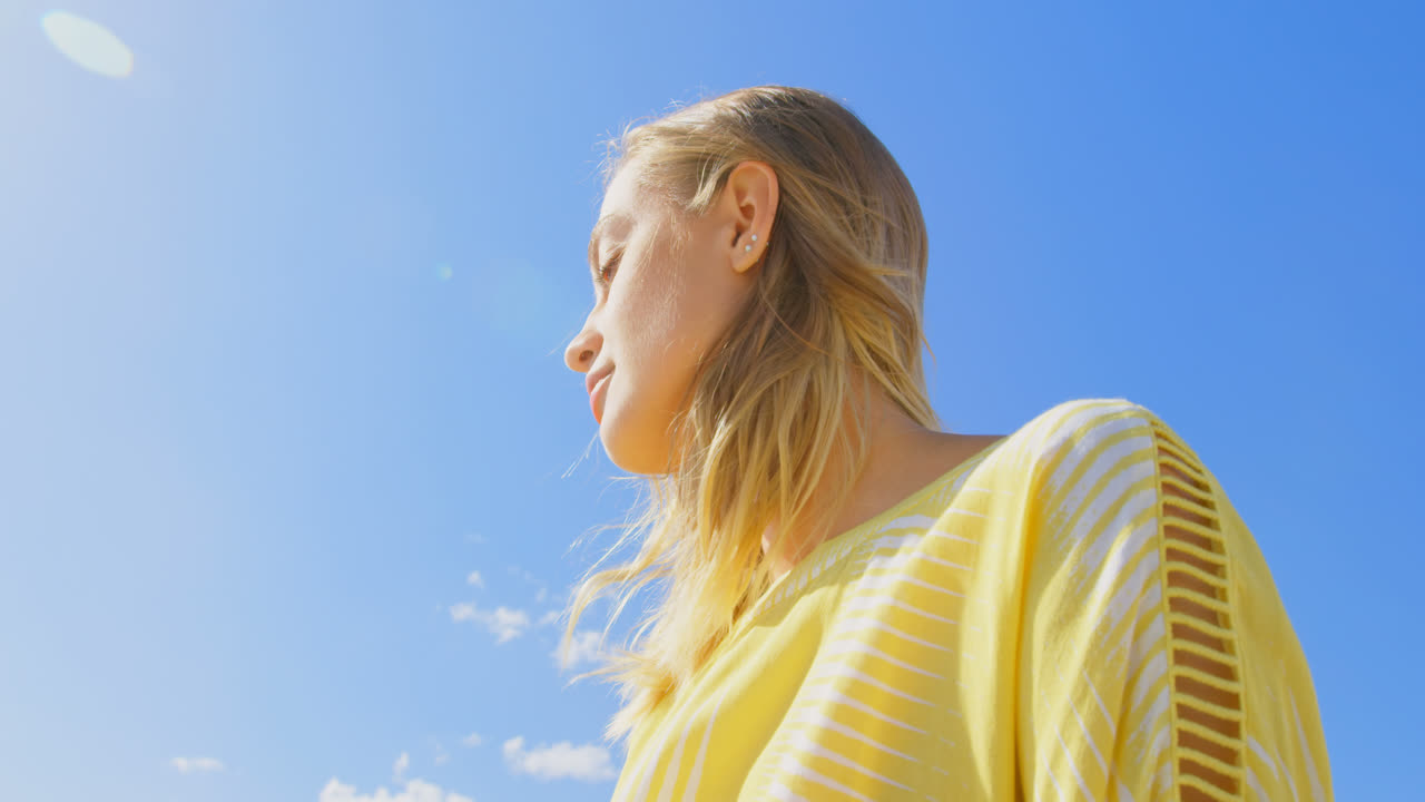 해변의 바위 위에서 휴식을 취하는 젊은 백인 여성의 낮은 각도 뷰 4k