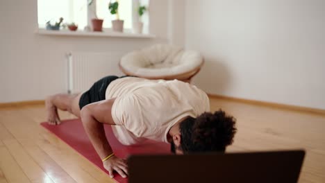 jeune homme travaillant à la maison dans son salon, faisant des pompes avec les jambes sur un tapis de yoga