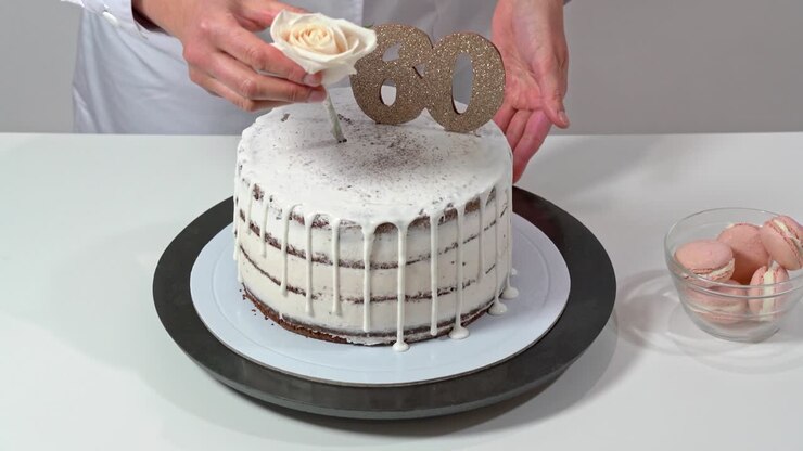 Chef finishing a birthday cake assembly by placing a rose as decoration final decoration. Celebrating sixty years of age.