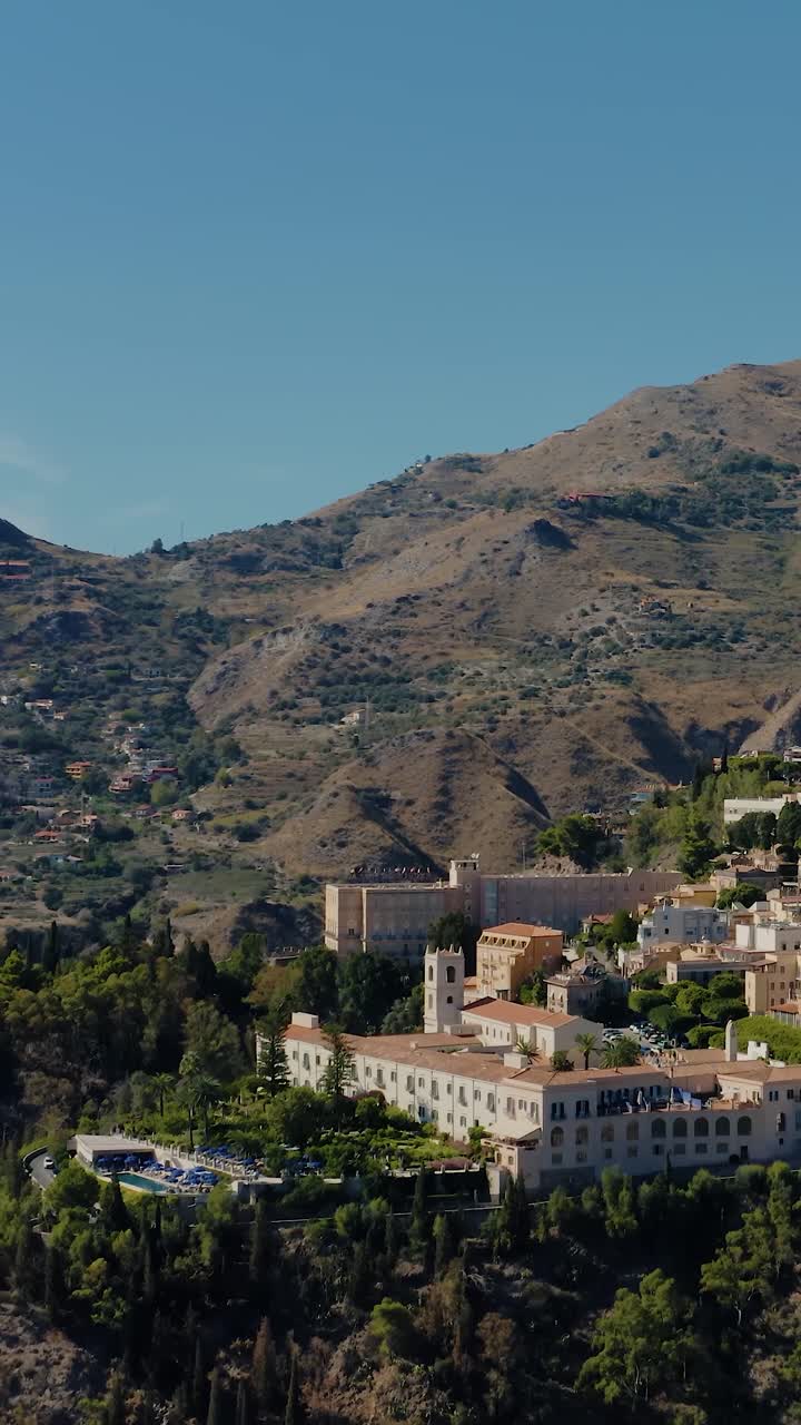 drone aéreo vertical disparado volando hacia la antigua ciudad de taormina en sicilia. espectacular vista de la aldea italiana en la cima de las montañas. destino de viaje más popular en sicilia