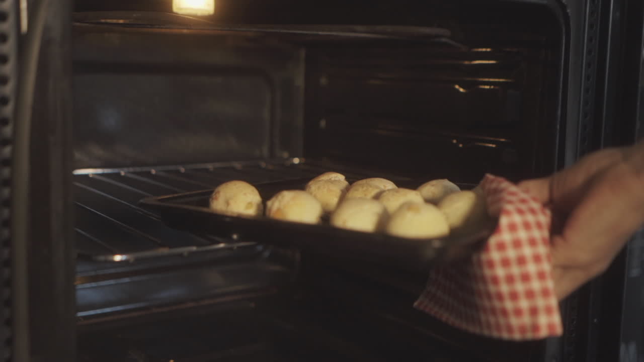 Persona saca una bandeja de pan de chipa recién horneado del horno, mostrando el proceso de horneado casero de este manjar tradicional