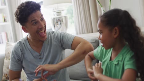 Happy-biracial-father-and-daughter-sitting-on-sofa-using-sign-language