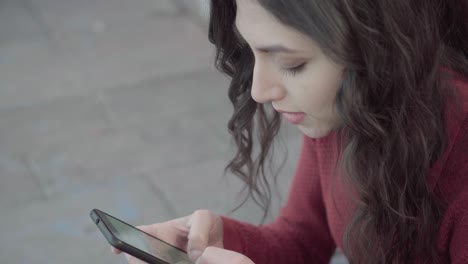 chica enviando mensajes de texto cerca de la pared de ladrillo estática de cerca
