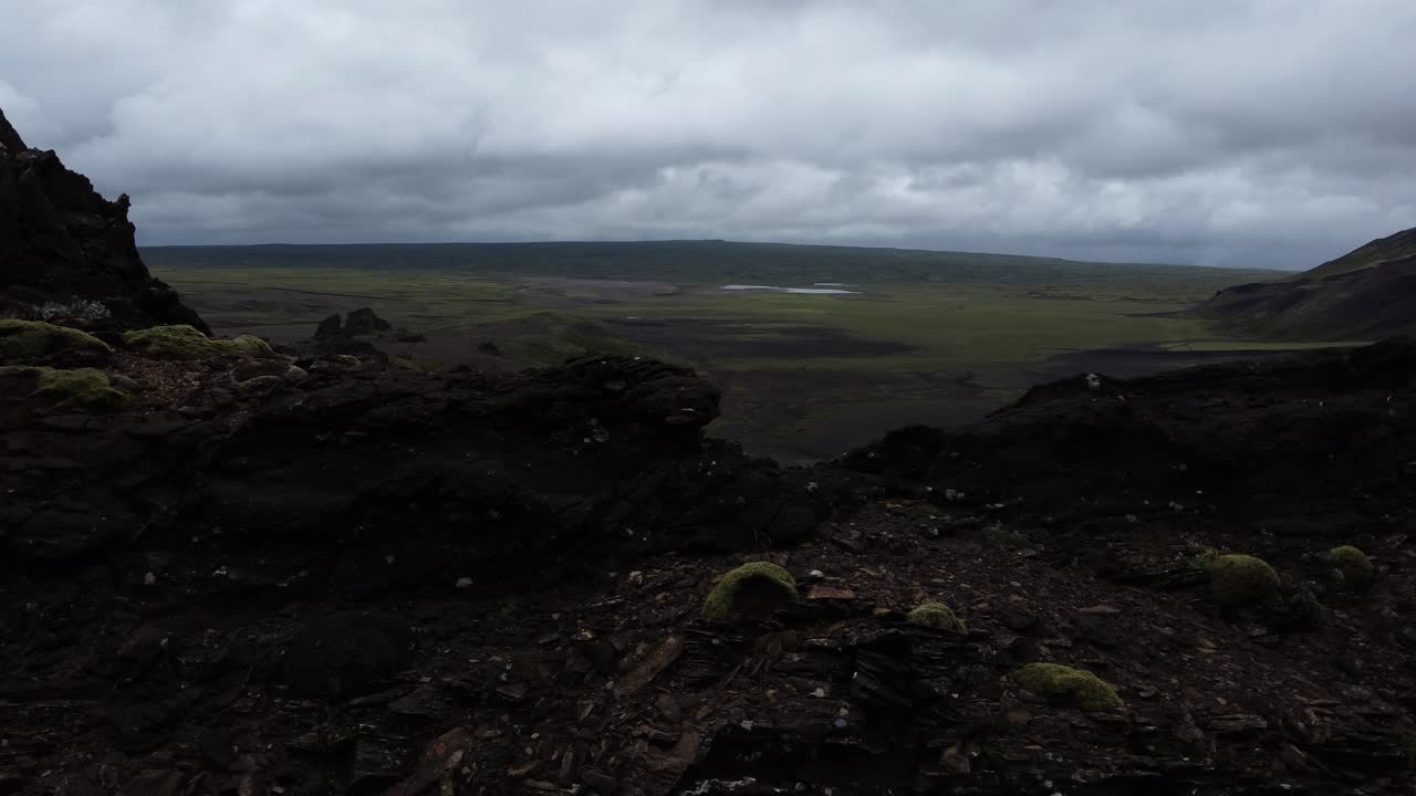 Aerial view of rugged volcanic terrain with scattered green patches and dark lava fields under cloudy sky in Icelandic highlands showing remote landscape and geological textures