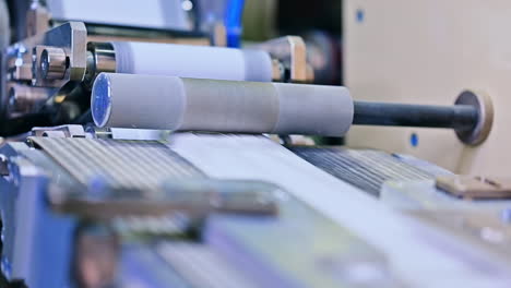 white ribbon passing under the metal roller. quick conveyor line at the diaper manufacturing factory. close up.