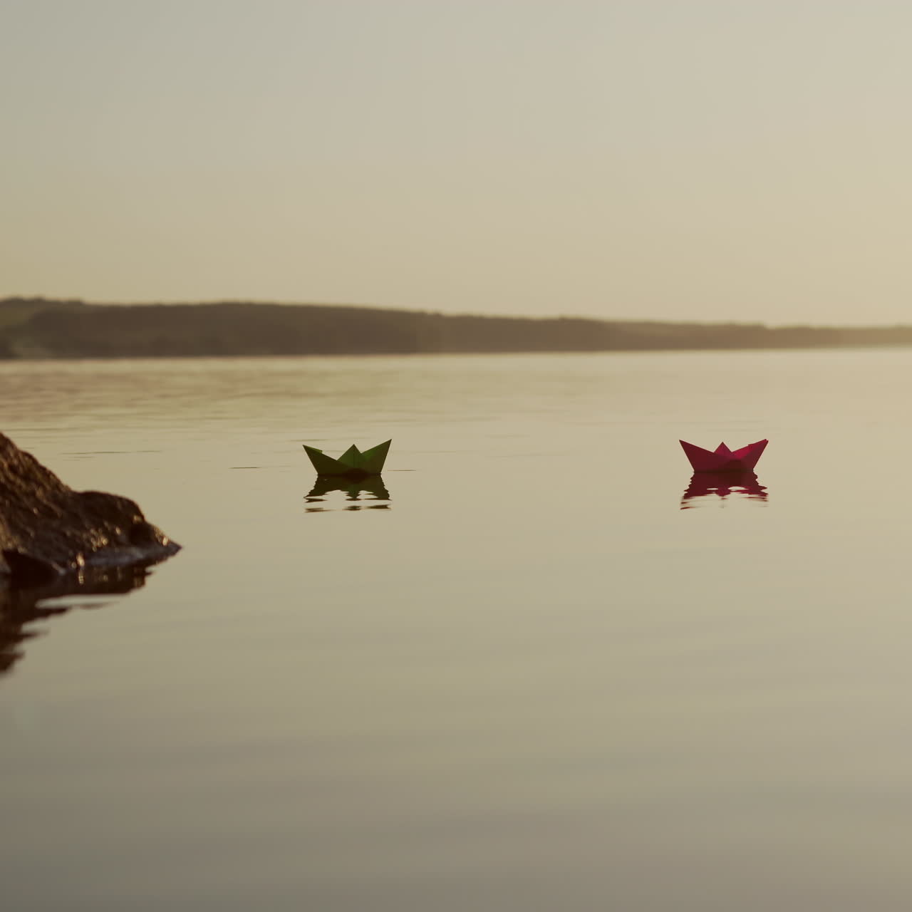 Paper boats swim at sunset. Evening water background and two origami ships floating. Dreams and future concept.