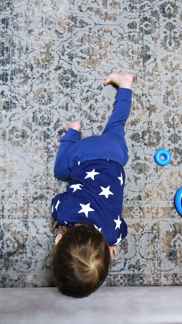 Little baby crawling by the carpet. Kid reaches his hand under the sofa and pulls the phone out. Child playing with gadget. Top view. Vertical video