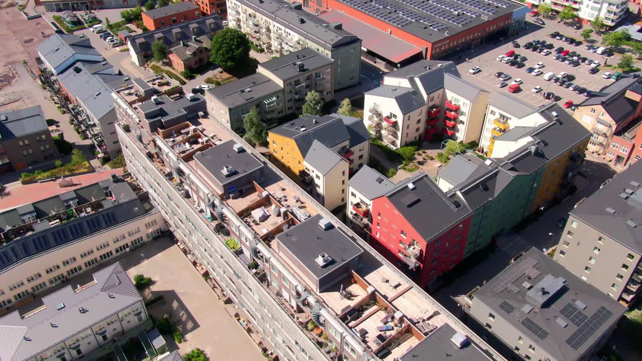 Luftfoto af farverige lejlighedsbygninger med varierende tage og parkeringsområder i Gustavsberg. Indfanger livlig svensk forstadsarkitektur