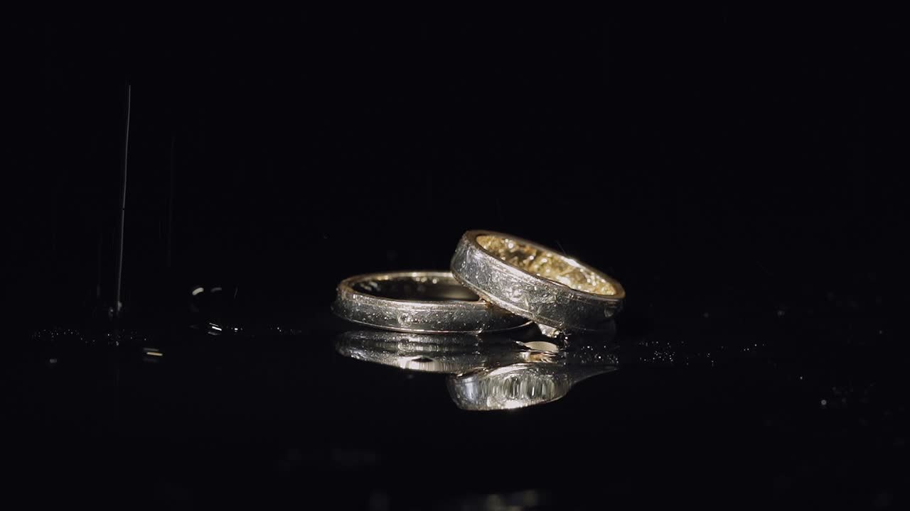 Wedding rings on dark water surface shining with light. Close up macro