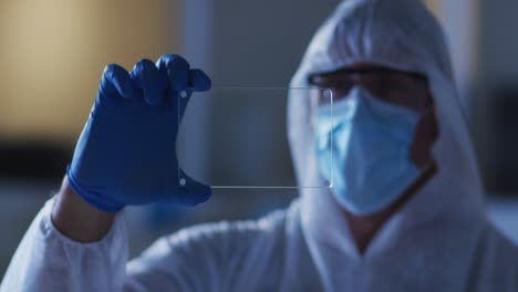 Caucasian-male-medical-worker-wearing-protective-clothing-and-gloves-using-handheld-interface-in-lab