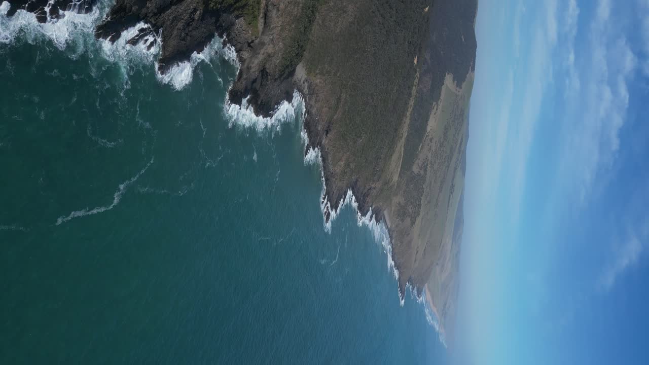 Aerial View of Rugged Coastline with Crashing Waves and Green Hills
