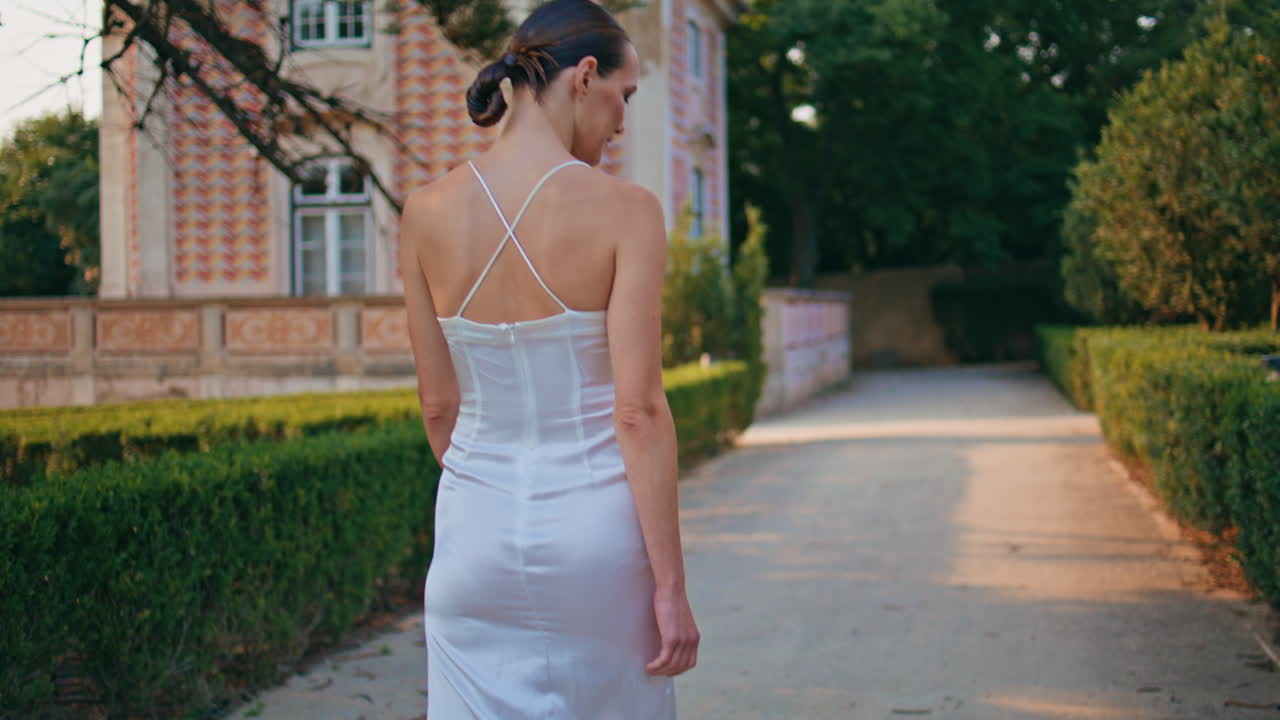 멋진 여자가 골목길을 걸어가며 미소 짓고 카메라를 향해 돌고 있다. 걸어가는 소녀