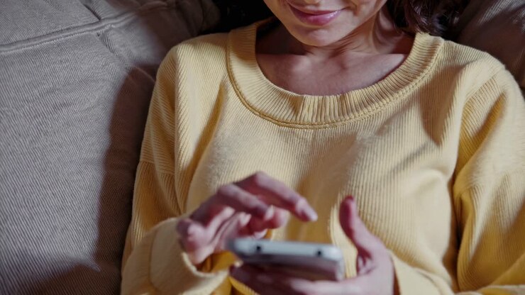 Close-up angle of a person in a yellow sweater using a smartphone, suggesting a relaxed, casual