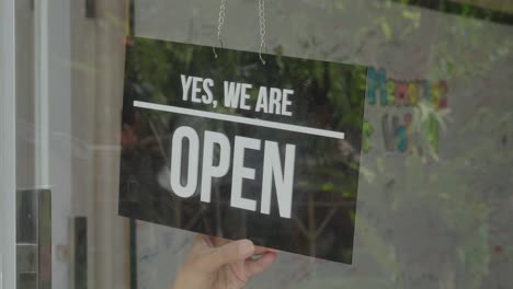 person changing the signboard with the inscription "closed" to "open" sign to welcoming customers