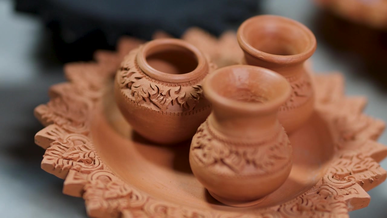 Primo piano di mani che sistemano intricate miniature di vasi in argilla su un piatto decorativo in ceramica in Thailandia