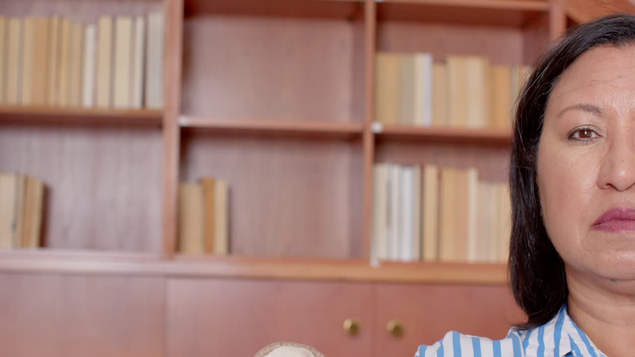 Senior woman sitting at home, relaxing in front of bookshelf, looking thoughtful, copy space