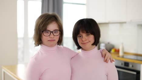 Portrait-of-two-cute-girls-with-down-syndrome-standing-together-embracing-at-home