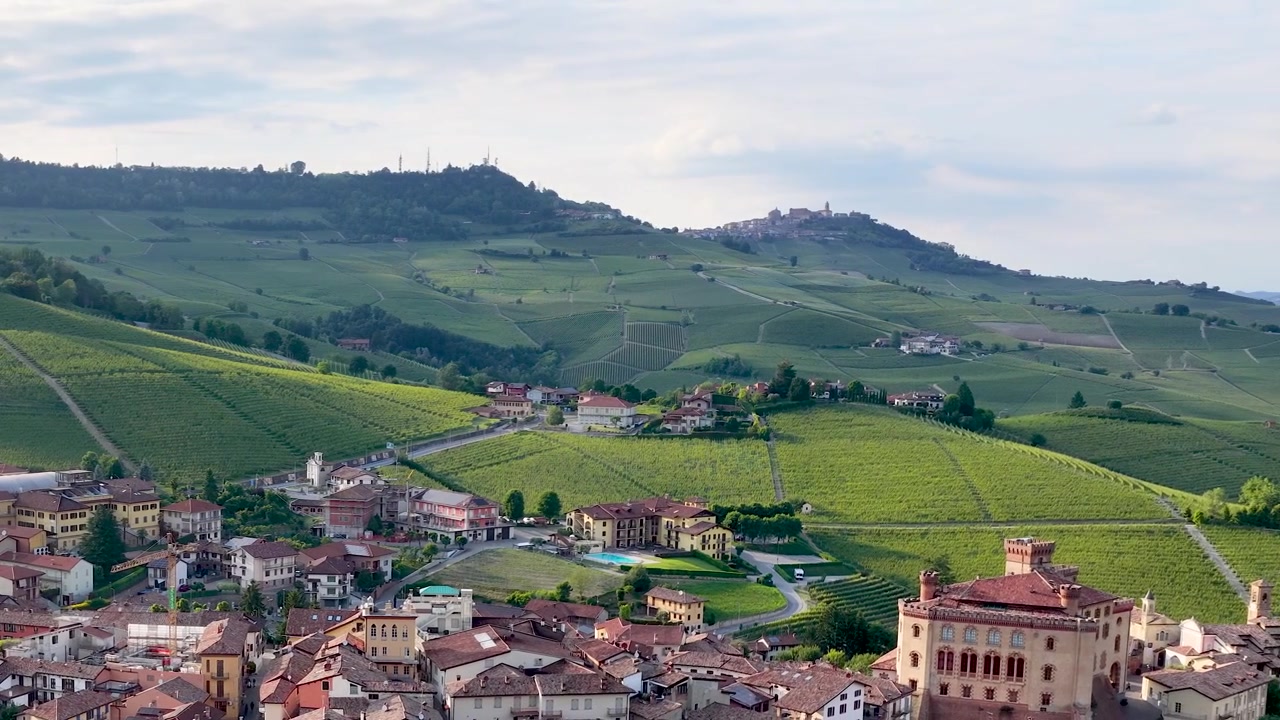 Ripresa panoramica con drone che attraversa lo storico villaggio di Barolo e le lussureggianti colline ondulate di vigneti in Italia.