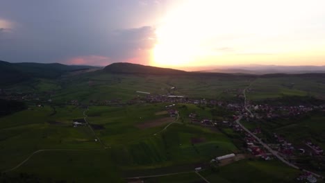 Amplia-Toma-Aérea-De-Una-Gran-Puesta-De-Sol-Sobre-Amplios-Campos-Y-Prados-Verdes-Cerca-De-Una-Desventaja,-Transilvania,-Rumania