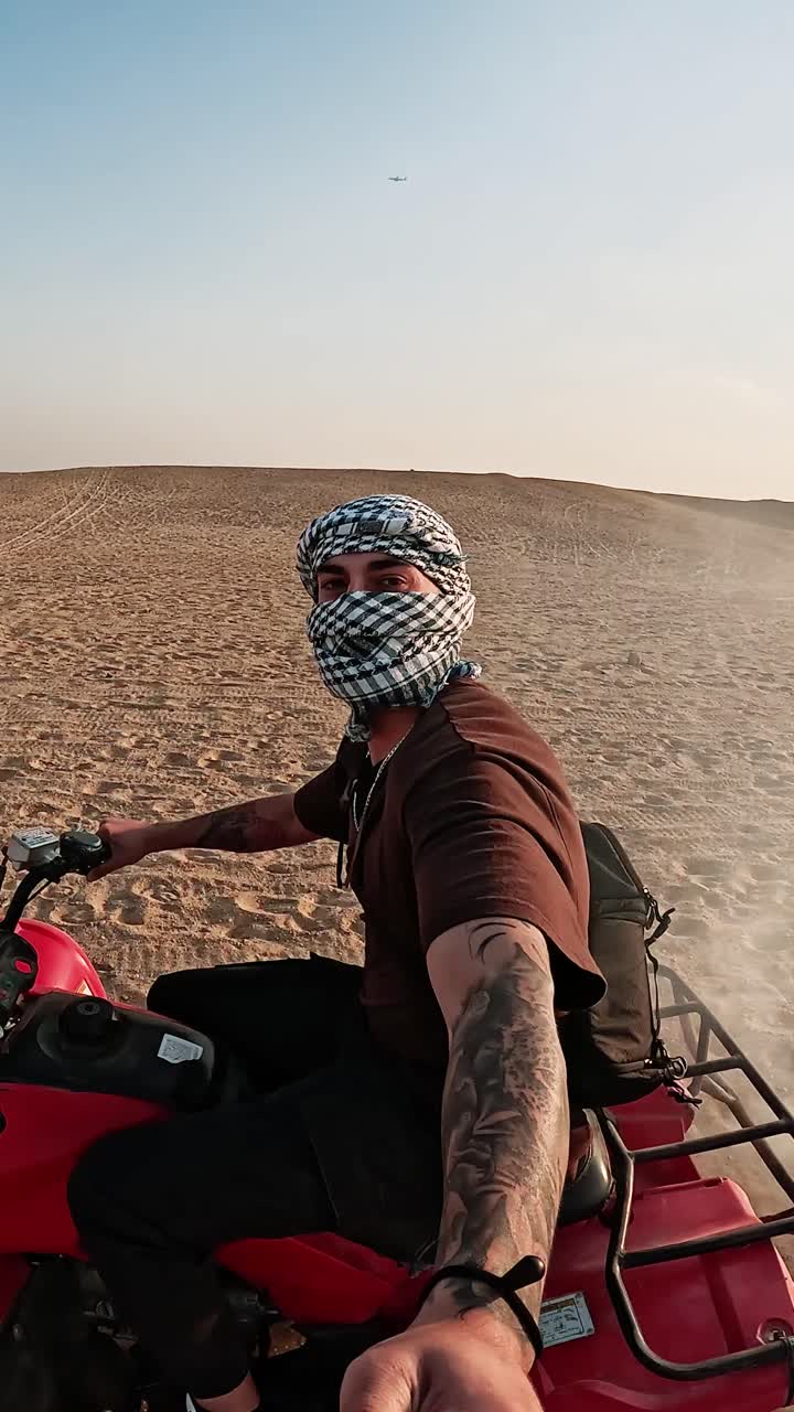Uomo con kefiah in quad nel deserto al tramonto