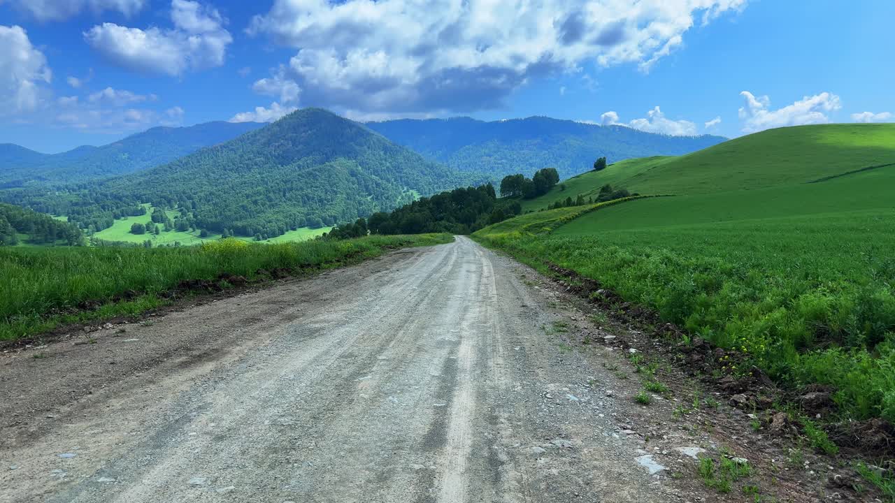 A Serene Country Road Embarking into a Beautiful Green Landscape Surrounded by Majestic Mountains and a Clear Blue Sky