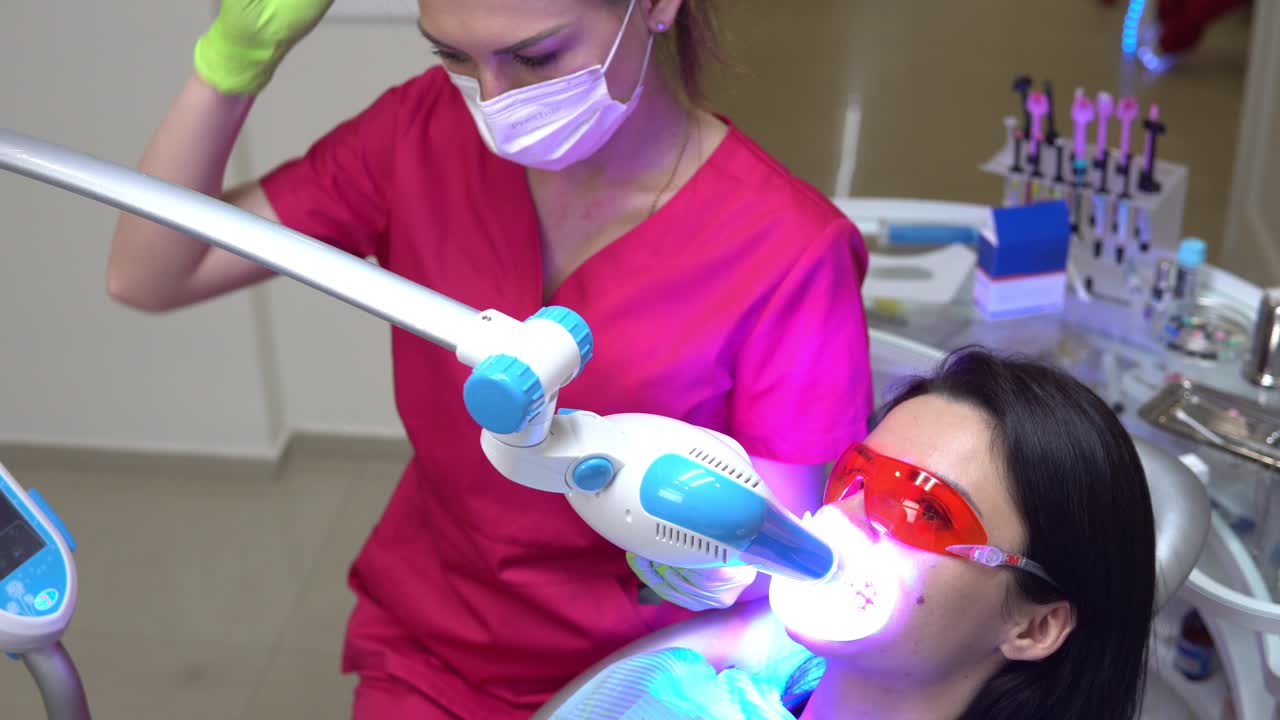 Young woman getting UV whitening at the dentist's office by an ultra violet machine. Shot in 4k