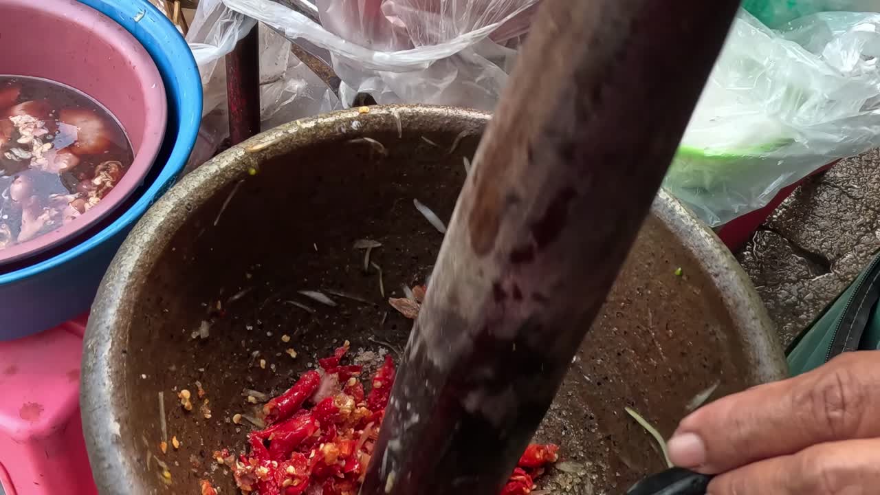 Close-up of hands using a pestle to crush red chilies in a stone mortar.