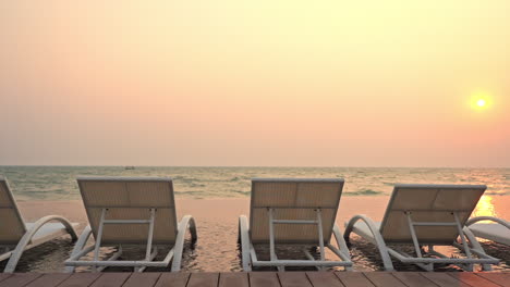 a row of beach loungers sits in shallow water facing the incoming tide at sunset