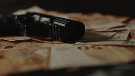 dolly of a pistol with the barrel pointed towards the camera laying on a pile of money