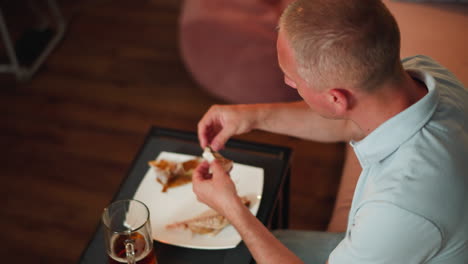 aerial view of man in light blue polo shirt seated indoors removing bone from smoked fish before eating, with glass of drink on table, showing careful preparation and relaxed home dining atmosphere