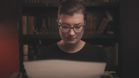 Dolly-shot-out-of-a-woman-typing-on-an-antique-typewriter-in-front-of-a-book-case