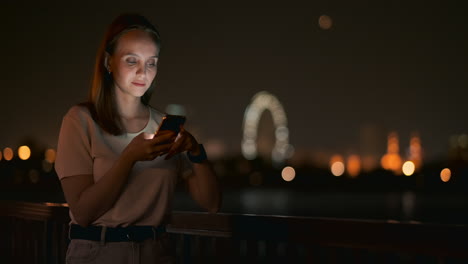 a beautiful young girl in the summer in a big night city keeps a smart phone in shell and writes a message reads e-mail and communicates in chat rooms and social networks keeps a blog looks at the phone screen