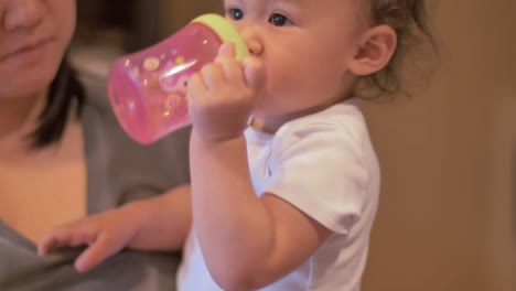 a toddler being held by her mom drinks out of her sippy cup