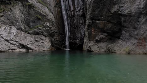 Lago-De-Montaña-Prístino-Con-Cascada,-Agua-Cayendo-En-Un-Profundo-Abismo-Oscuro