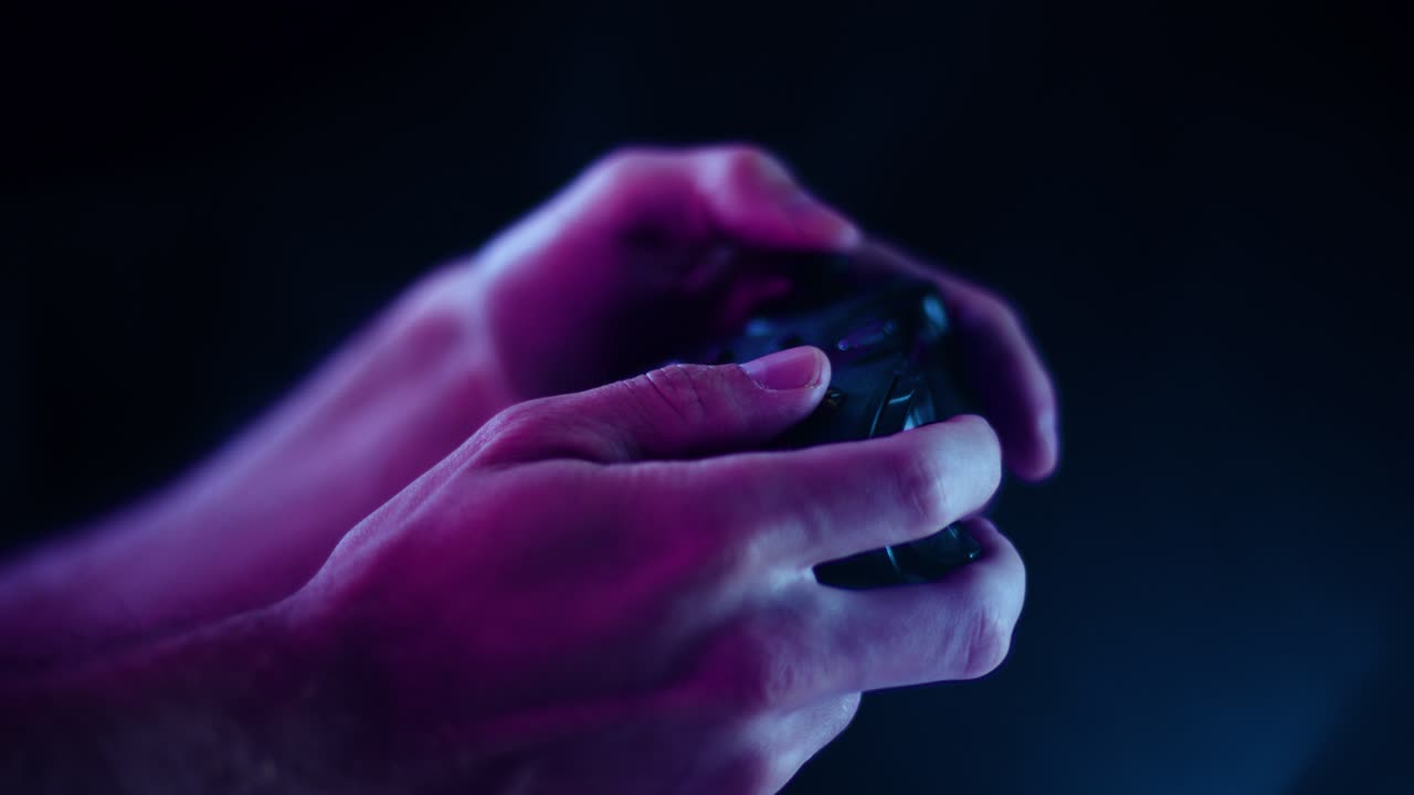 Playing video games in a darkened room with a black background close up on a controller buttons playing quickly blue lens flare