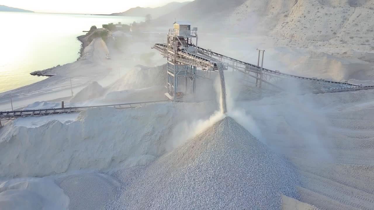Aerial shot of conveyor belt offloading plaster and revealing ocean in background.