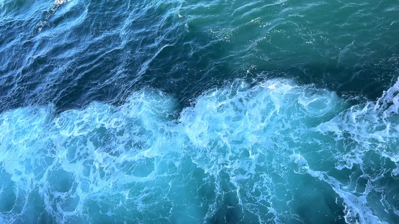 Wake of ferry ship with blue sea and white waves in sunshine and shadow.