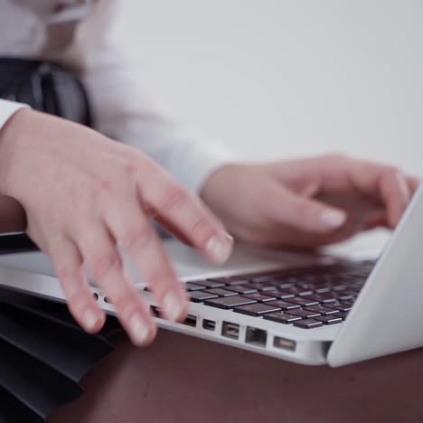 Modern laptop on female's legs. Young woman's hands typing on a white laptop. Close-up. Slow motion.