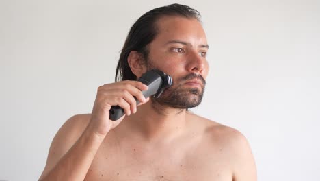 A-man-is-using-electric-shaver-to-trim-mustache-and-beard-while-standing-in-front-of-mirror-in-bathroom-at-home,-lather